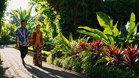 couple walks through lush tropical garden in traditional attire