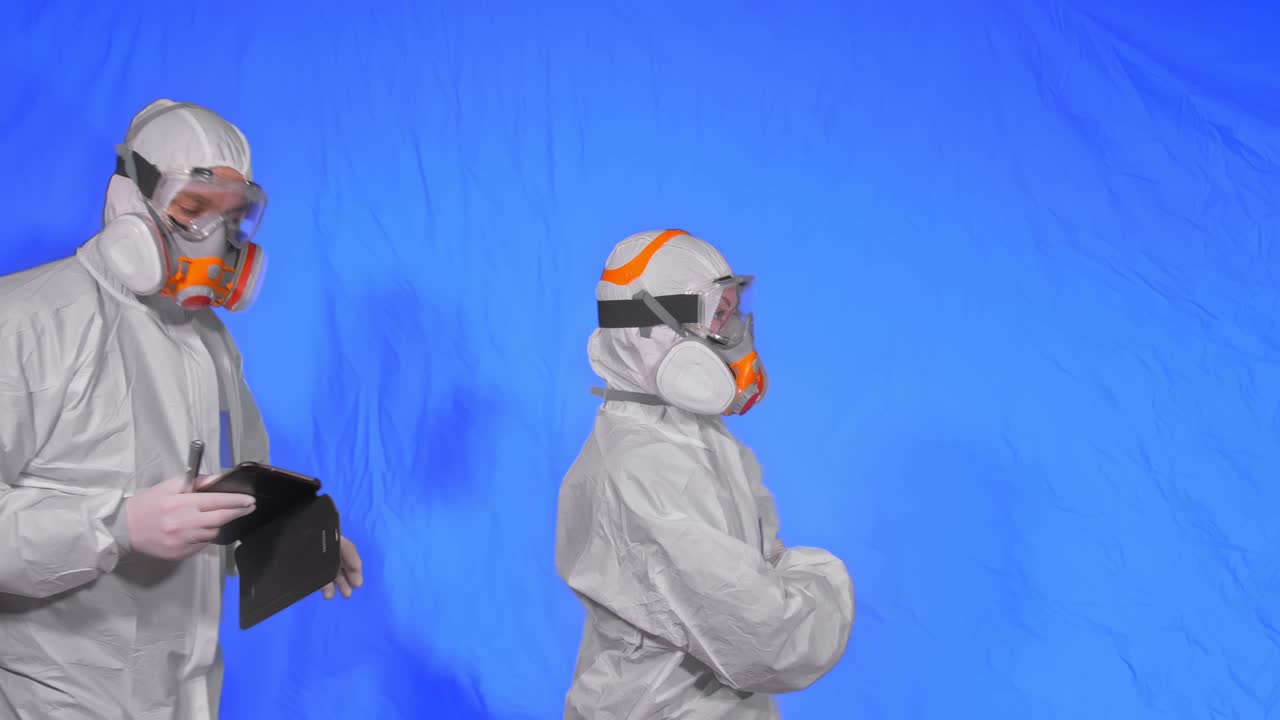 científico virólogo en respirador hace escribir en una tableta con lápiz. hombre y mujer con máscara médica protectora. clave de croma azul.