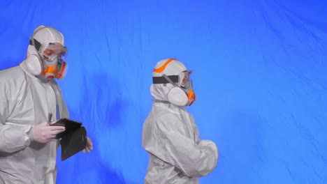 científico virólogo en respirador hace escribir en una tableta con lápiz. hombre y mujer con máscara médica protectora. clave de croma azul.
