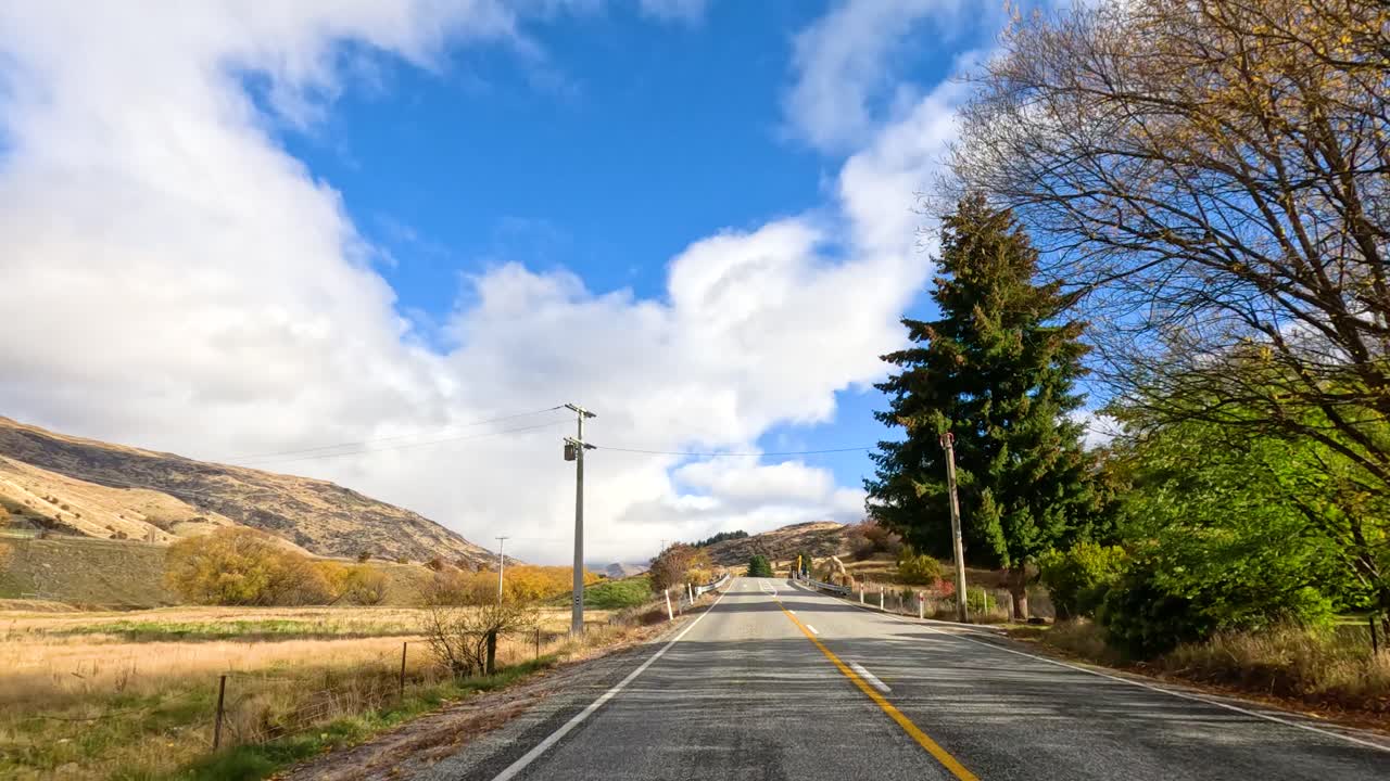 A serene drive through New Zealand's countryside, showcasing vibrant autumn colors, clear skies, and winding roads