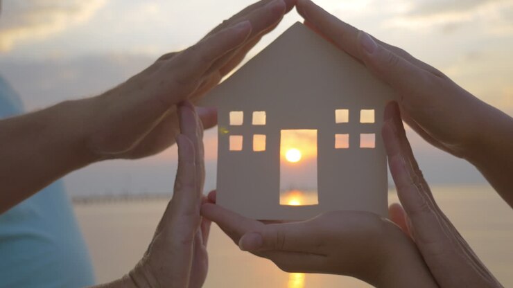 Hands Holding House Silhouette against Sun