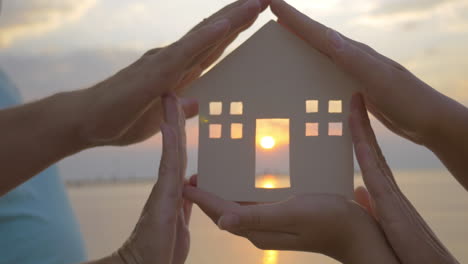 hands holding house silhouette against sun