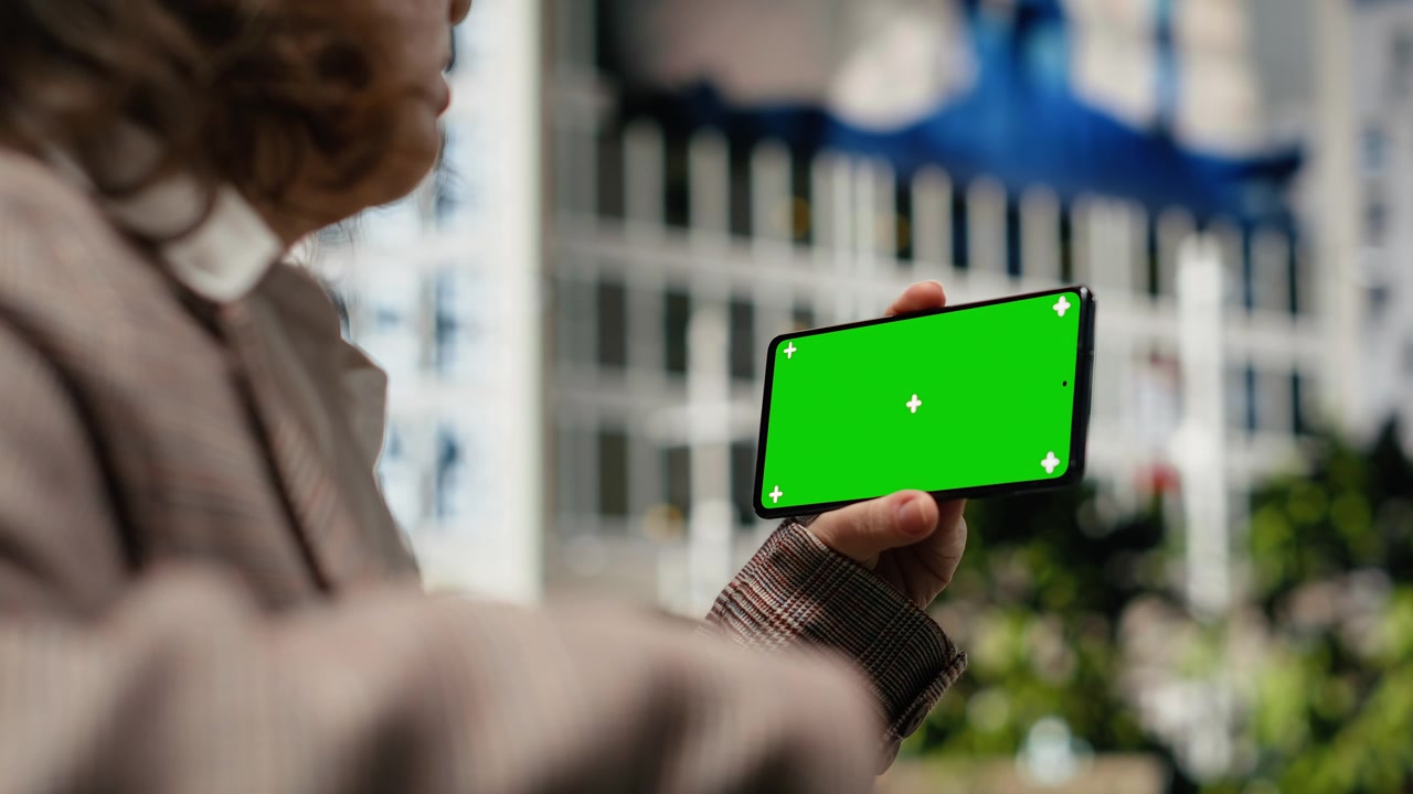 Primo piano di smartphone con schermo verde tenuto da una donna su una panchina del parco.