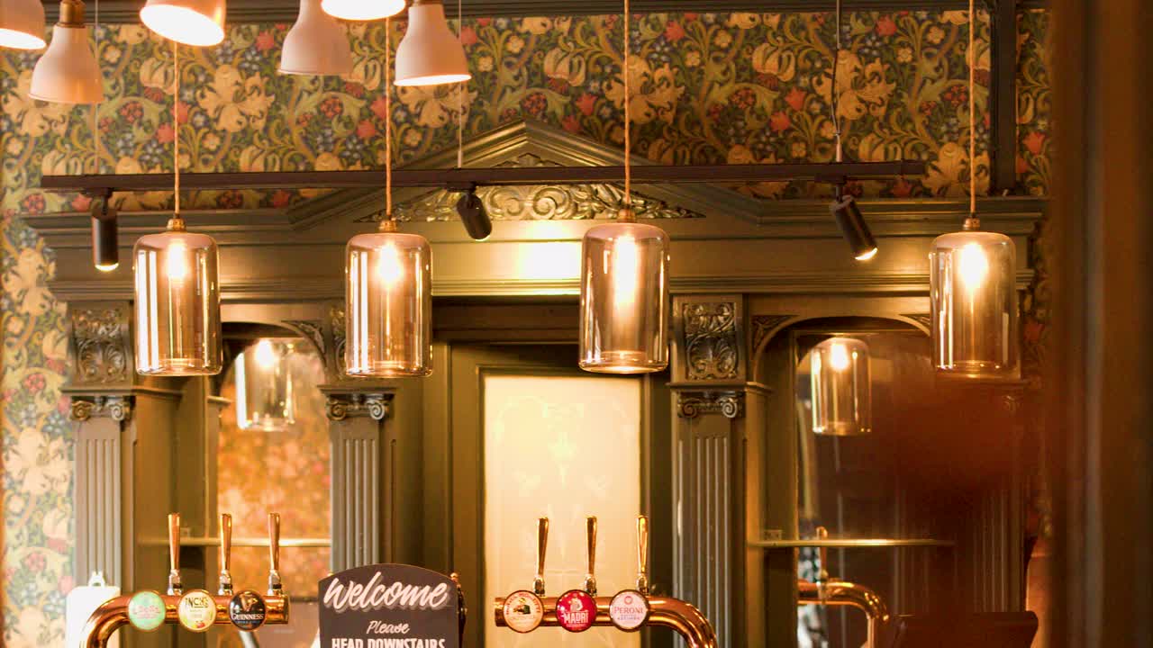 A hand glides over a warmly lit vintage pub bar with ornate decor and classic beer taps