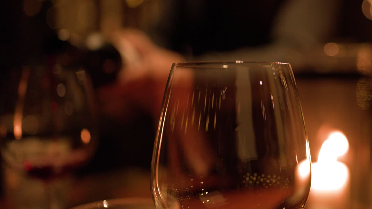 Primo piano di vino rosso versato in un bicchiere durante una cena intima a lume di candela