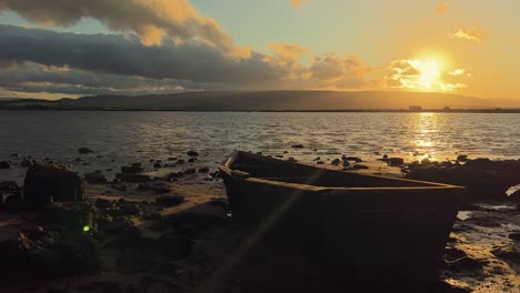 Time-lapse-De-Un-Pequeño-Barco-En-Una-Orilla-Tranquila-Con-El-Sol-Poniéndose-Detrás-De-Nubes-Dispersas