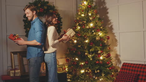 una pareja intercambiando regalos cerca del árbol de navidad.