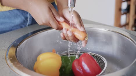 sección media de una mujer afroamericana enjuagando verduras en el fregadero de la cocina, en cámara lenta