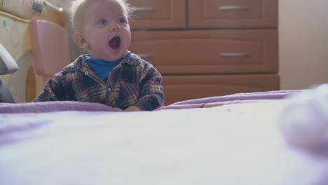 little baby climbs up on large bed with pink blanket in room