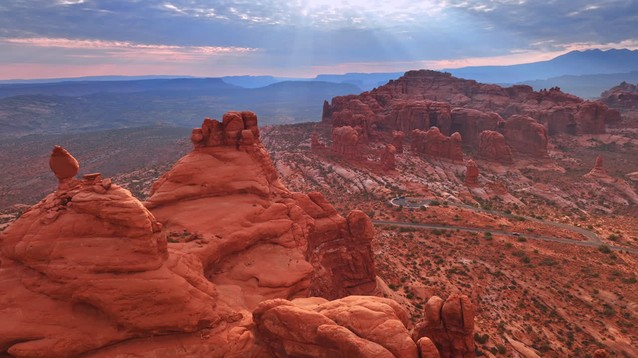 Avvicinamento alle cime delle rocce rosse modellate in modo bizzarro dall'erosione eolica. I raggi del sole al tramonto attraversano le nuvole. Il Parco nazionale degli Arches, USA. Vista aerea