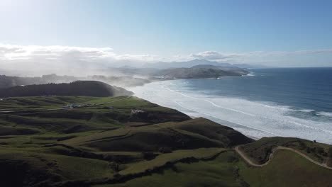 winding coastline with misty hills and crashing waves. scenic view of praia do castelejo in algarve, portugal. the lush green hills lead down to the ocean with powerful waves crashing onshore