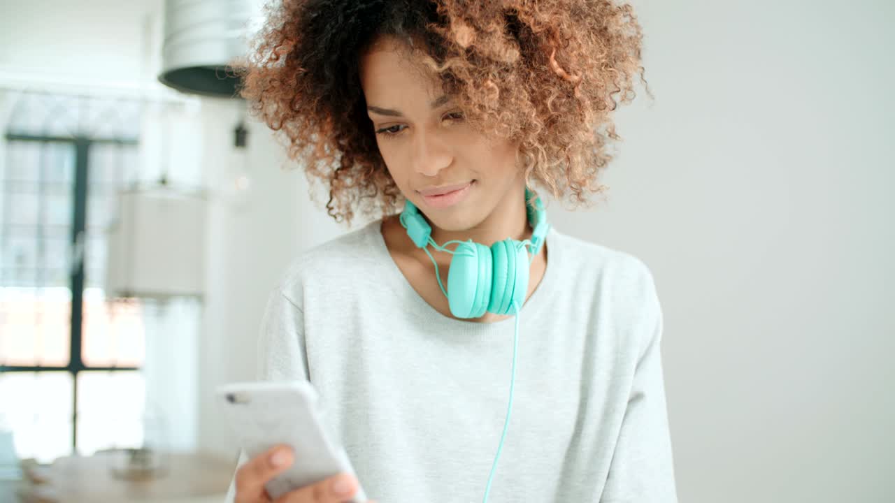 Bella giovane donna afroamericana che messaggia al cellulare a casa.