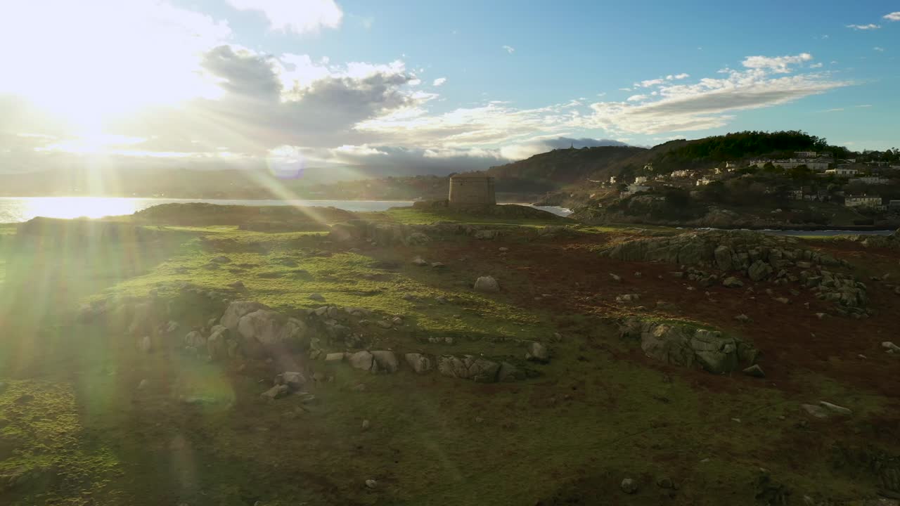 Dalkey Island, Dublin, Ireland, January 2020. Drone orbits Martello Tower tracking past grassy stone outcrops with views of St. Begnet's Church, Killiney Hill, and Wicklow Mountains on the horizon.