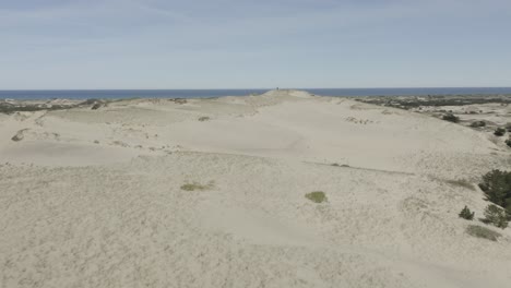 Drone-shot-flying-forwards-over-some-dunes,-with-2-people-standing-on-a-high-dune-in-the-distance