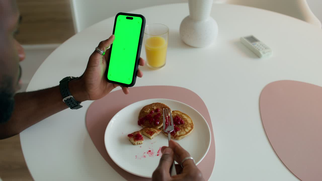 hombre tomando el desayuno mientras usa un teléfono con una pantalla verde