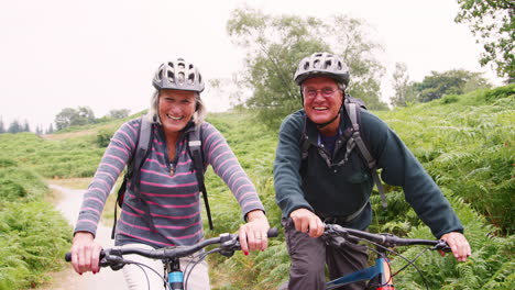 Senior-couple-sitting-on--mountain-bikes-in-the-countryside-during-a-camping-holiday,-Lake-District,-UK