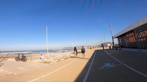 Zwei-Befreundete-Frauen-Genießen-Einen-Gemütlichen-Spaziergang-Entlang-Der-Ufermauer-Mit-Atemberaubender-Aussicht-Auf-Den-Strand,-Den-Sand-Und-Die-Wellen