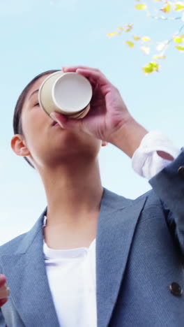 woman sipping coffee outside and using smartphone