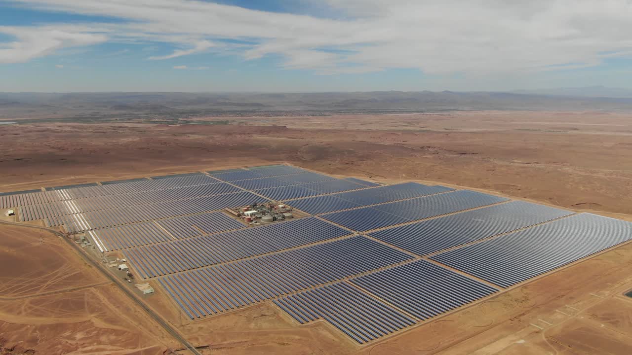 Luftfoto af en stor solcellepark i Ouarzazate, Marokko, der viser infrastruktur for fotovoltaisk energiproduktion i et ørkenlandskab.