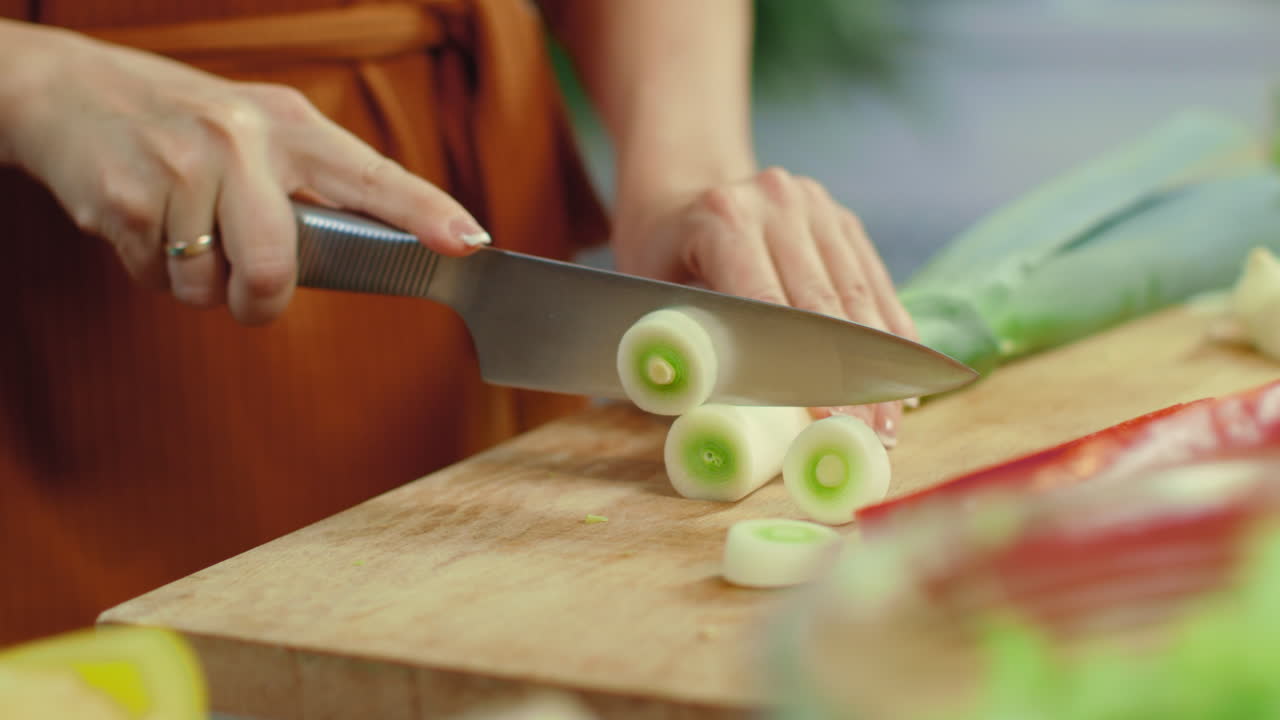 manos femeninas cortando puerro verde. niña preparando un plato vegetariano saludable.