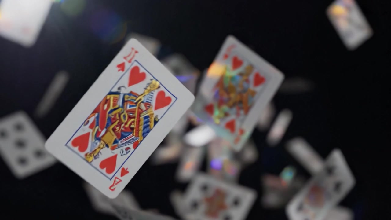 Spektakularny pokaz spadających kart do gry uchwycony w ruchu, ukazujący żywą sztukę i teatralność gier karcianych w dramatycznym oświetleniu.