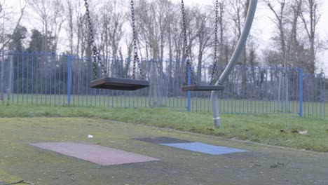 empty swinging swing on children playground with no people on a cloudy cold day in central london