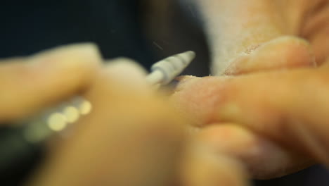 female manicurist using portable electric nail drill at beauty salon