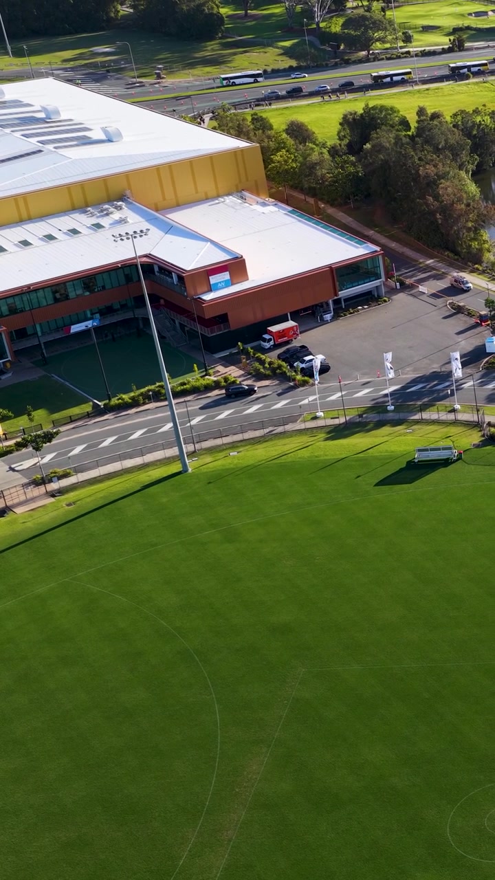 Droneoptagelse fra høj vinkel panorerer hen over en frodig grøn sportsbane og et moderne atletikanlæg