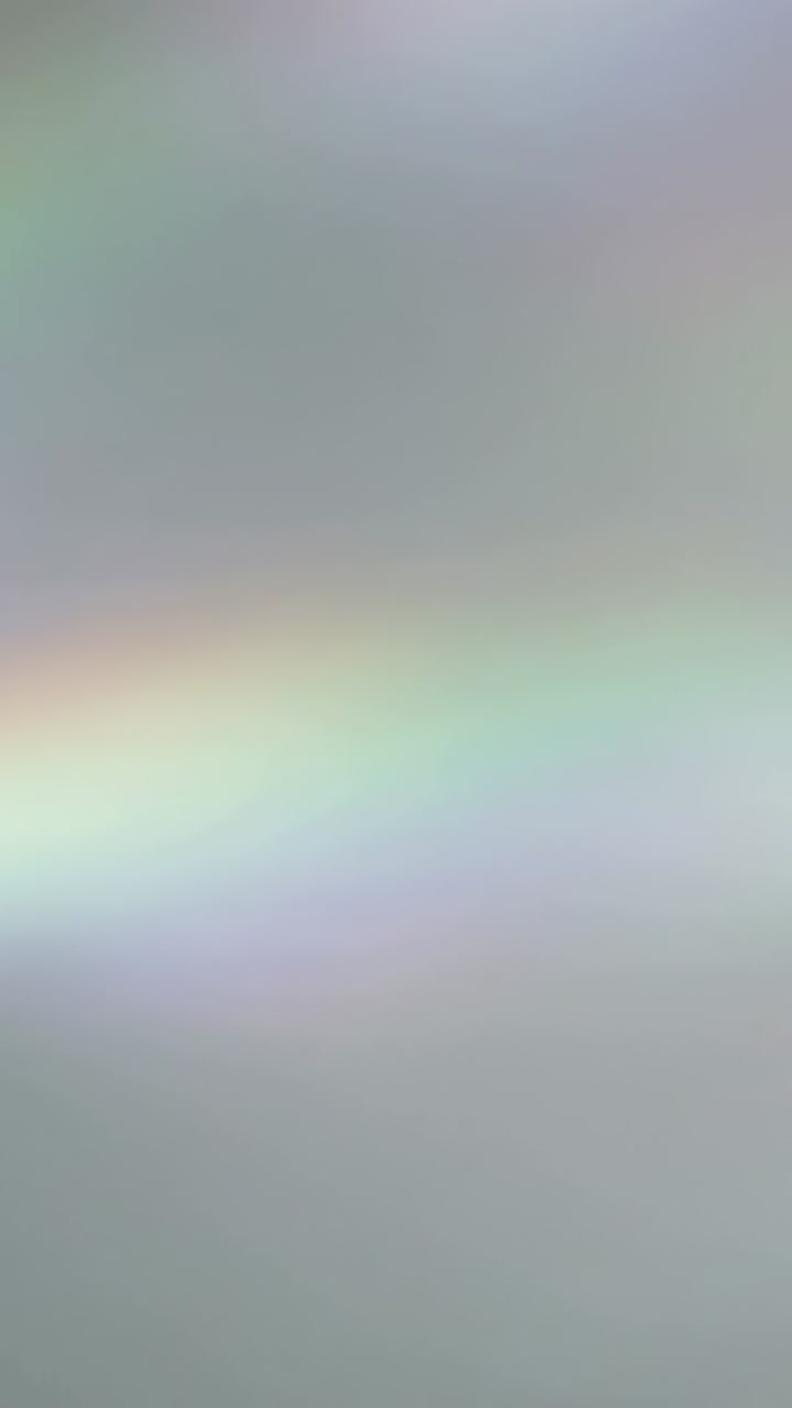 Vertical video: Shifting light angle moving pastel rainbow arc across studio wall, soft glow