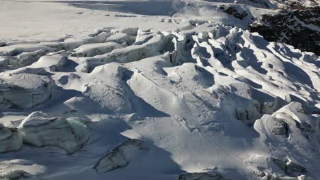 Toma-Panorámica-Aérea,-Llanura-Cubierta-De-Nieve-En-Los-Alpes-Suizos-Con-Un-Glaciar-Y-Sus-Grietas