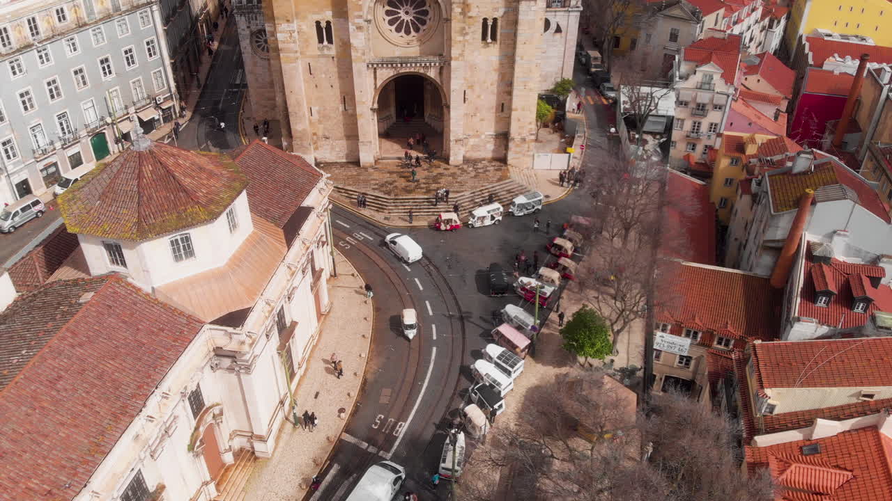 Drone trækker sig tilbage fra Sé de Lisboa med et nedadgående tilt, der afslører de omkringliggende gader og tage i Lissabon, Portugal.