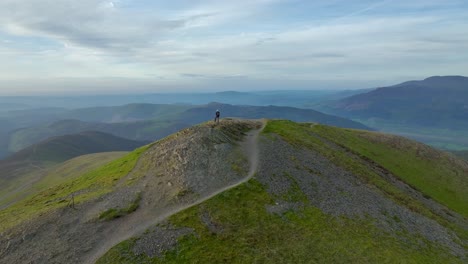 Lone-mountain-walker-at-winding-path-end-on-fell-summit-at-golden-hour