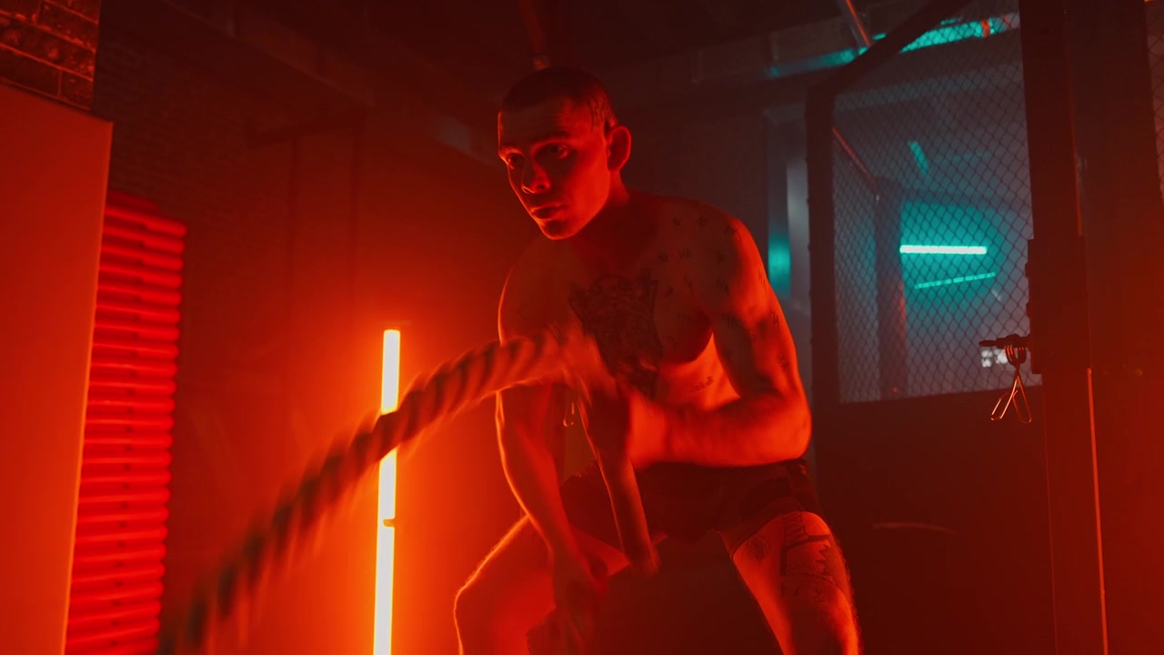 Uomo muscoloso che esegue un allenamento con le battle rope con illuminazione drammatica.