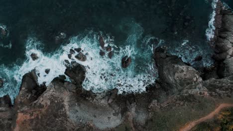 ascend top aerial drone view of waves crashing on rocky coastline