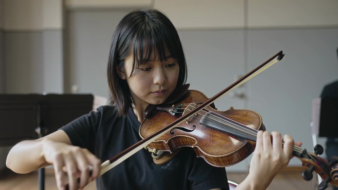 Playing female violinist in black T-shirt drawing bow across strings in rehearsal room, with violin
