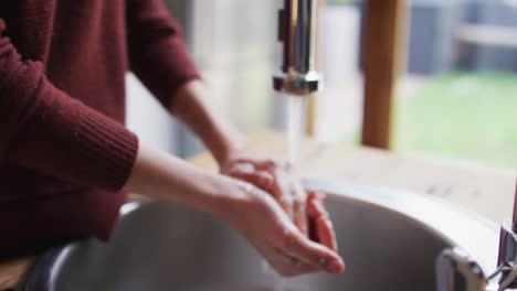 Mid-section-of-woman-washing-her-hands-in-the-sink-at-home