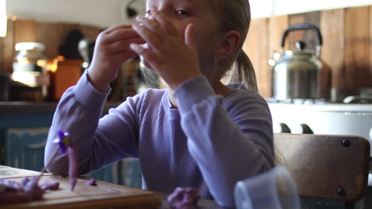Close up footage of a young five year old girl playing with clay in the kitchen of the house she lives in