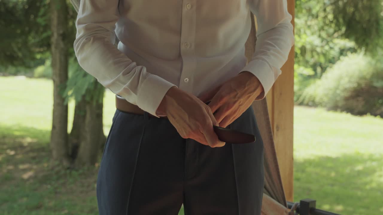 Groom getting dressed by fastening his belt. Slow motion close up