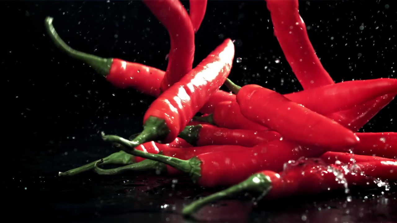 Peperoncini rossi freschi che schizzano acqua su sfondo nero