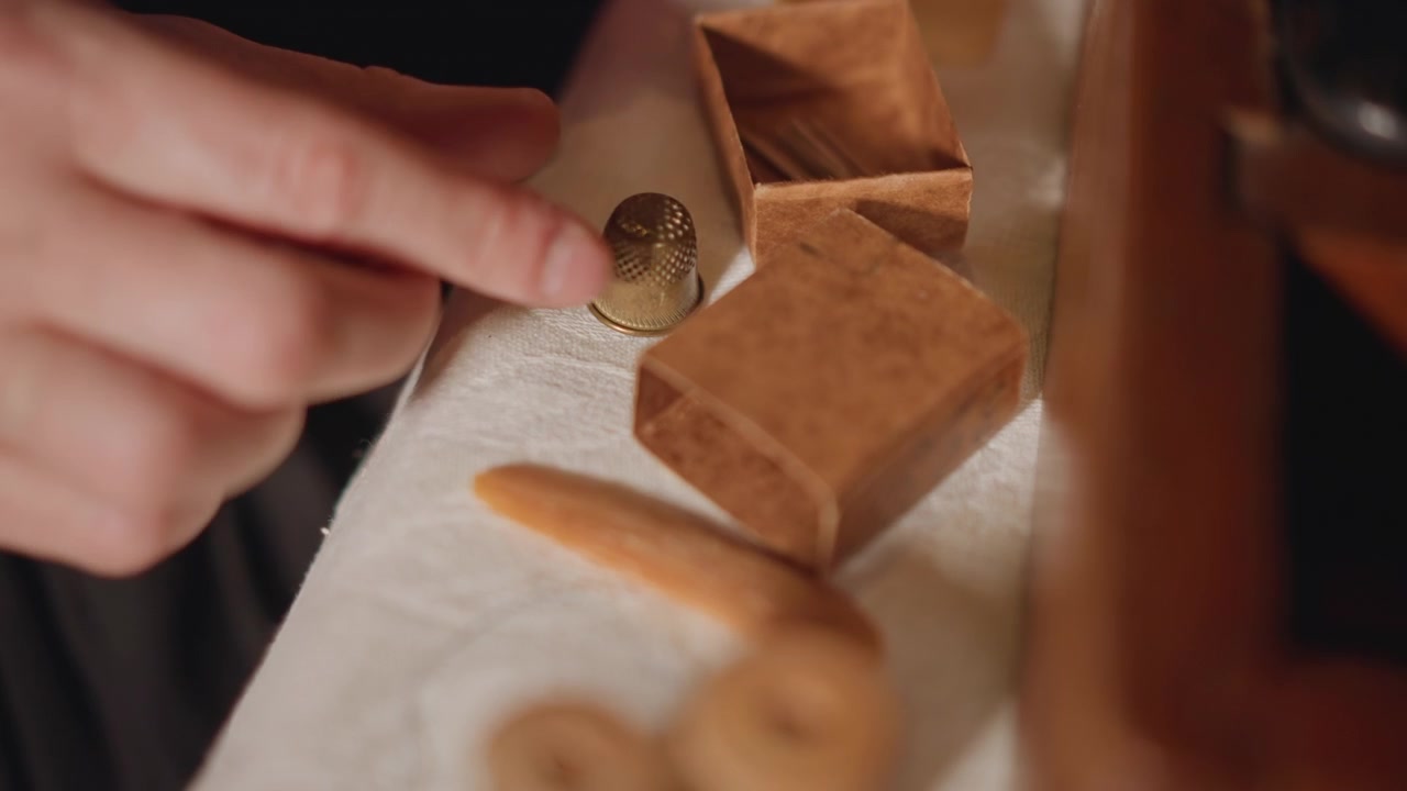 Mani organizzano piccoli oggetti. Un individuo ordina con cura bottoni e spilli sul tavolo da lavoro. Un artista separa e posiziona diligentemente strumenti di cucito in miniatura su delicato materiale di pizzo in un laboratorio.