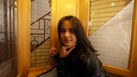 Pretty-Woman-in-an-Old-Vintage-Elevator,-Black-Leather-Coat,-Handbag,-Long-Black-Hair,-Attractive,-Europe