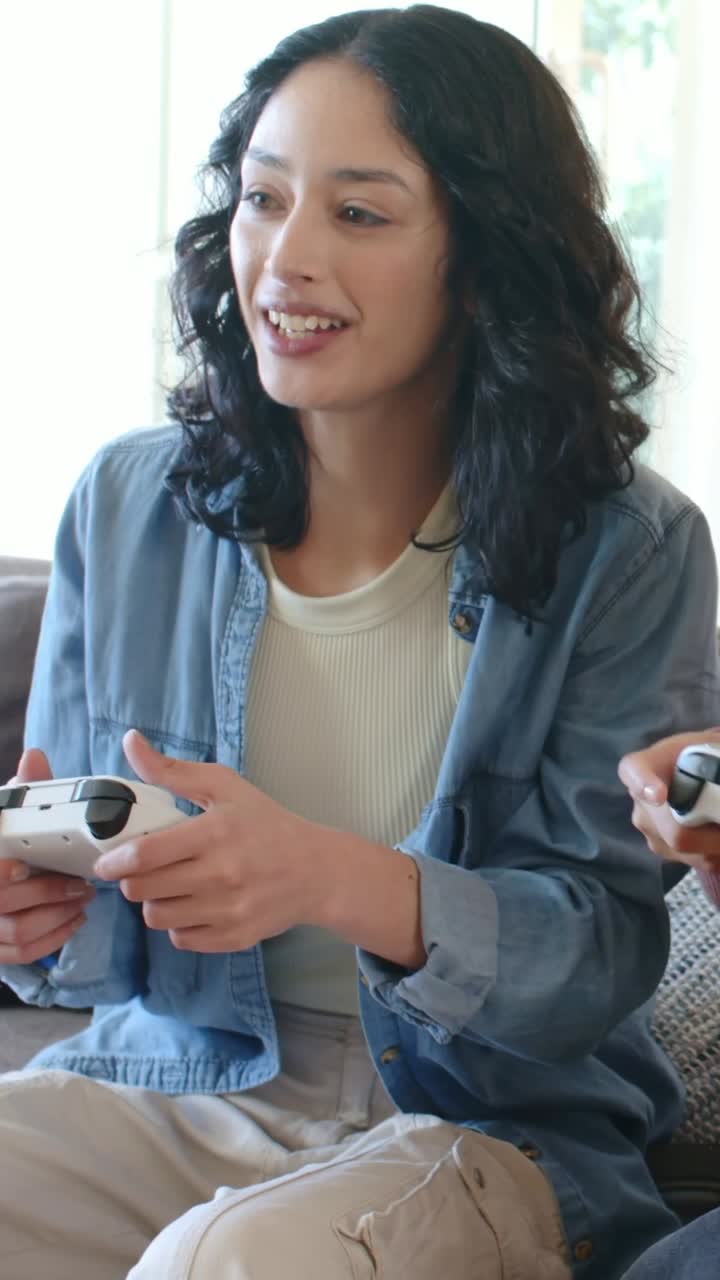 Vertical video: Game cue woman in blue top pressing white controller on couch rust-top raising it