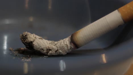 closeup cigarette burn out in blue ashtray, time lapse