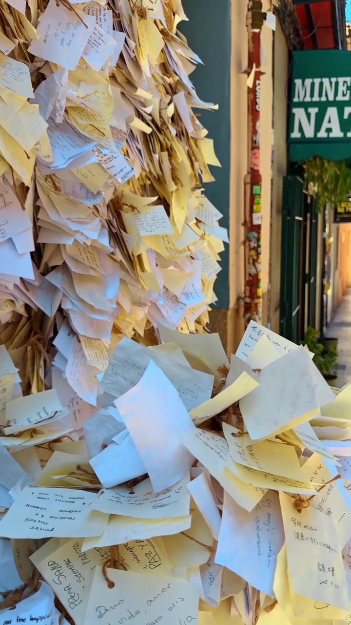 Madrid, Spain, 8 August 2025: Close-up of wall covered in handwritten paper notes. Dense texture of many small white and yellow paper notes pinned or tied to a wall with handwriting.