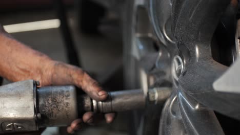 Mecánico-De-Automóviles-Latinos-Usando-Herramientas-Como-Pistolas-De-Impacto-Neumáticas-Para-Apretar-Los-Pernos-De-Las-Ruedas-Del-Carro-En-El-Garaje-De-Reparación-De-Automóviles-Mexicano---Cámara-Lenta-De-Cerca