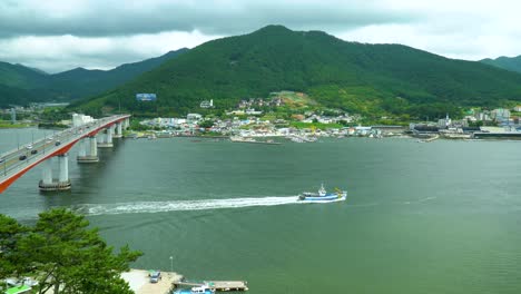 new geoje grand bridge with vehicles travelling to tongyeong and a ship crossing the coastal area with view of lush green mountain in geojedo island, south korea