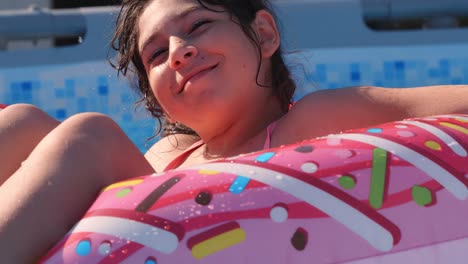 11-12 años feliz chica caucásica linda acostada en un círculo de rosquilla inflable en la piscina en un jardín. vacaciones de verano frescas para niños y niños. juegos en el agua. donat rosa. 4k cámara lenta
