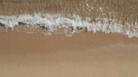 Top-down-ascending-footage-of-crystal-clear-water-on-beach.-Waves-washing-sand-on-coast.-Barcelona,-Spain