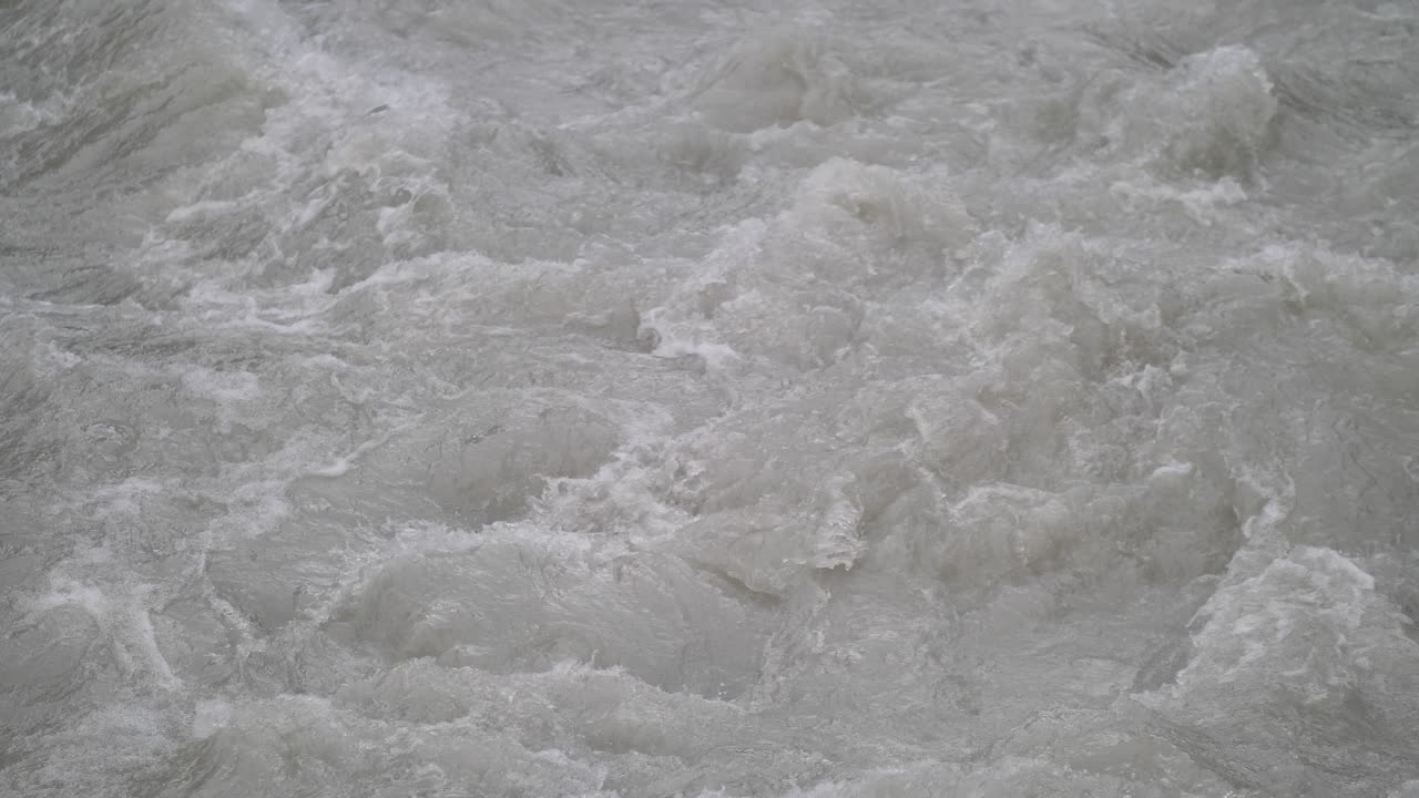 Fast streaming gray melted water in a small river and sloshing on the rocks and stones in Lauterbrunnen Switserland. Close-up shot