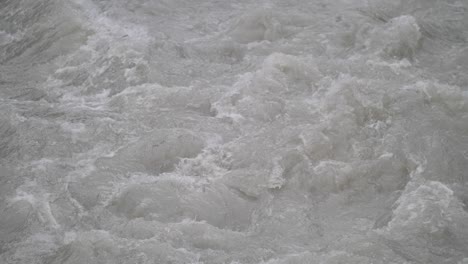 fast streaming gray melted water in a small river and sloshing on the rocks and stones in lauterbrunnen switserland. close-up shot
